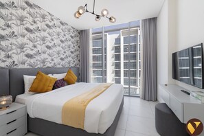A modern bedroom with a large bed, a TV, and a balcony with city views.