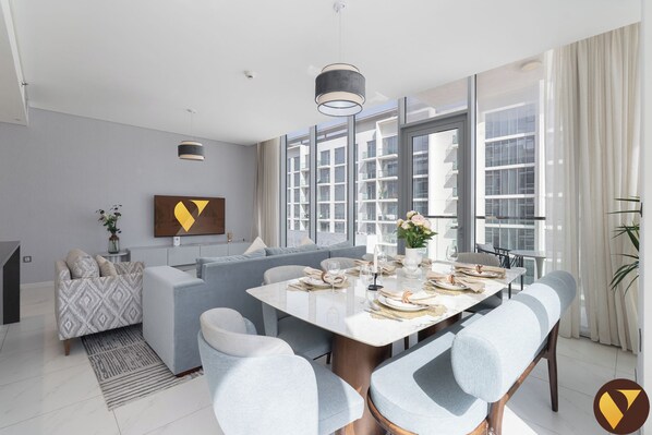 A modern dining area with a white table, grey upholstered chairs, and a grey sofa.