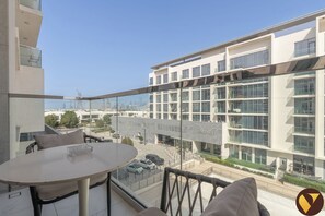 A modern building with a glass facade, a balcony with a table and chairs, and a view of the cityscape.