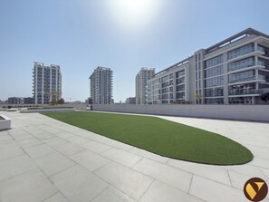 A modern residential complex with multiple high-rise buildings, a rooftop garden, and a clear sky.