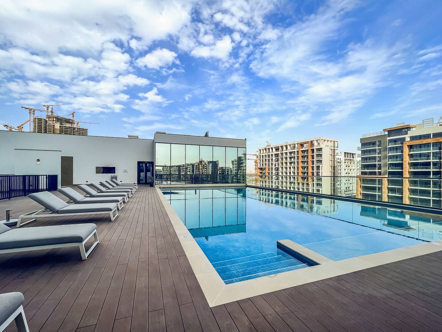 Una piscina en la azotea con sillones de descanso y vistas a la ciudad.