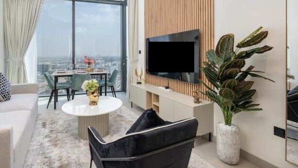 Una sala de estar moderna con un televisor grande, una zona de comedor con mesa y sillas, y un ventanal con vistas a la ciudad.
