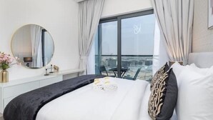 Habitación de hotel moderna con una cama grande, un espejo redondo, vistas a la ciudad y un balcón con mesa y sillas.