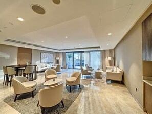 Eine großzügige Hotelhalle im modernen Stil mit einer breiten Sitzgelegenheit, bestehend aus Sofas und Sesseln, einem Esstisch und einem großen Fenster mit Blick auf die Stadt.