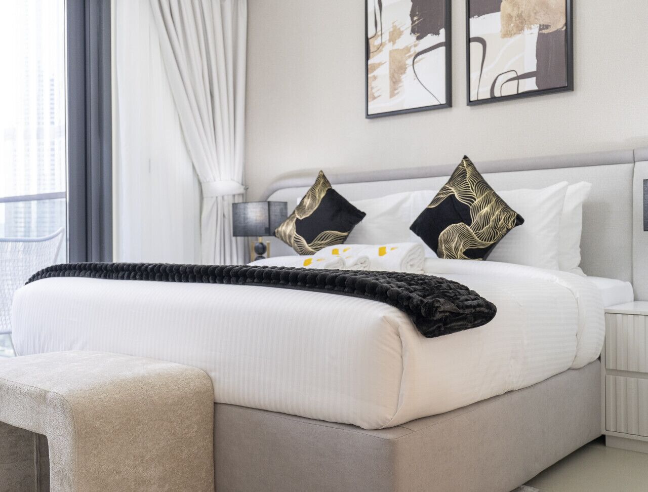 Quarto moderno com uma cama grande, mesa de cabeceira e janela com cortinas.