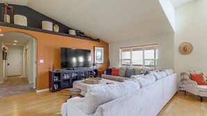 Un salon spacieux avec un grand canapé d’angle, un téléviseur à écran plat et un plancher en bois.