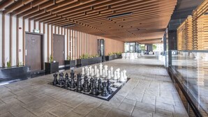 Um hall espaçoso com um grande tabuleiro de xadrez no chão, teto de painéis de madeira e design arquitetônico moderno.