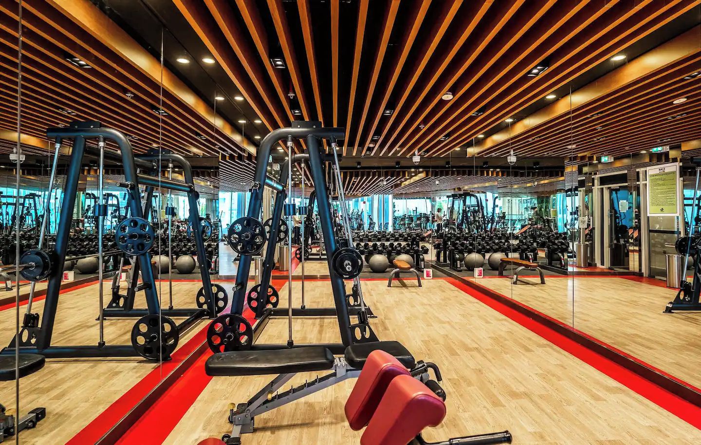 Un gimnasio con diversos equipos de ejercicio, suelo de madera y alfombra roja.