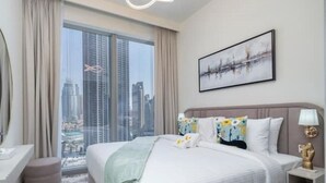 Ein modernes Hotelzimmer mit einem großen Bett, Blick auf die Stadt, einem gerahmten Kunstwerk und einem Nachttisch mit Lampe.