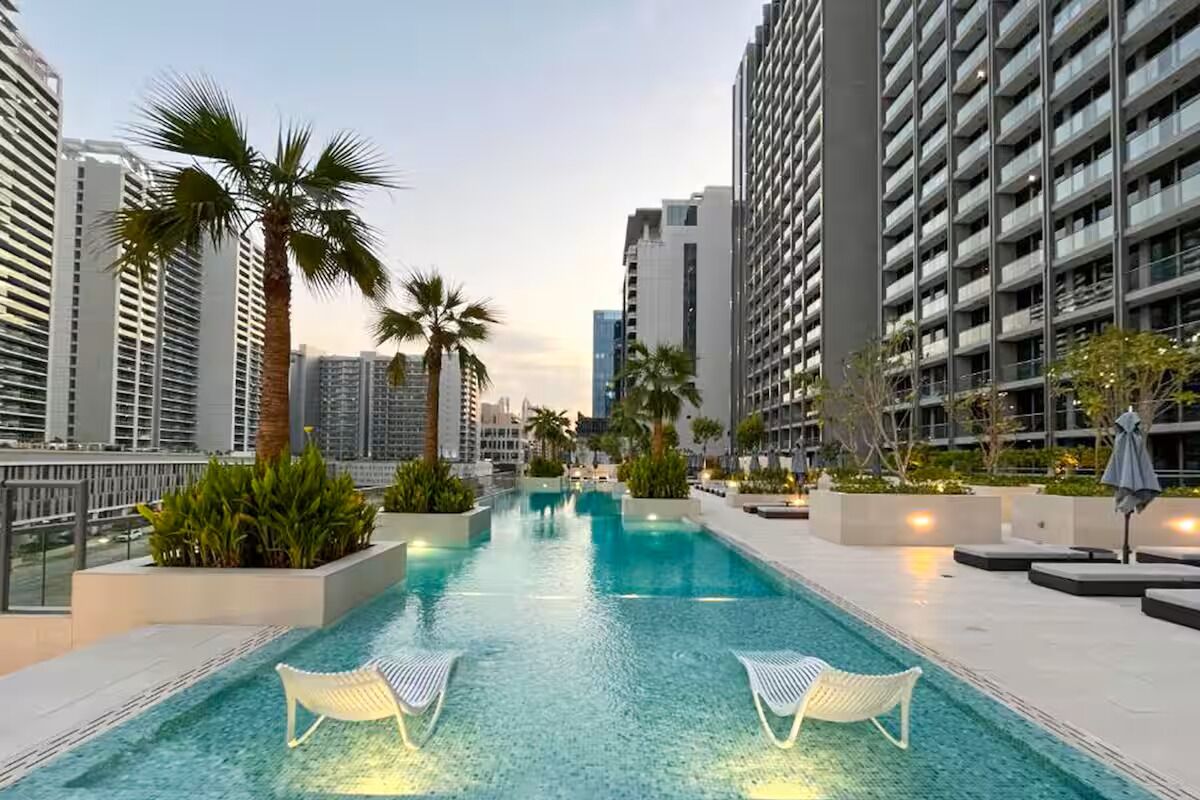 A rooftop swimming pool with lounge chairs, surrounded by high-rise buildings and palm trees.