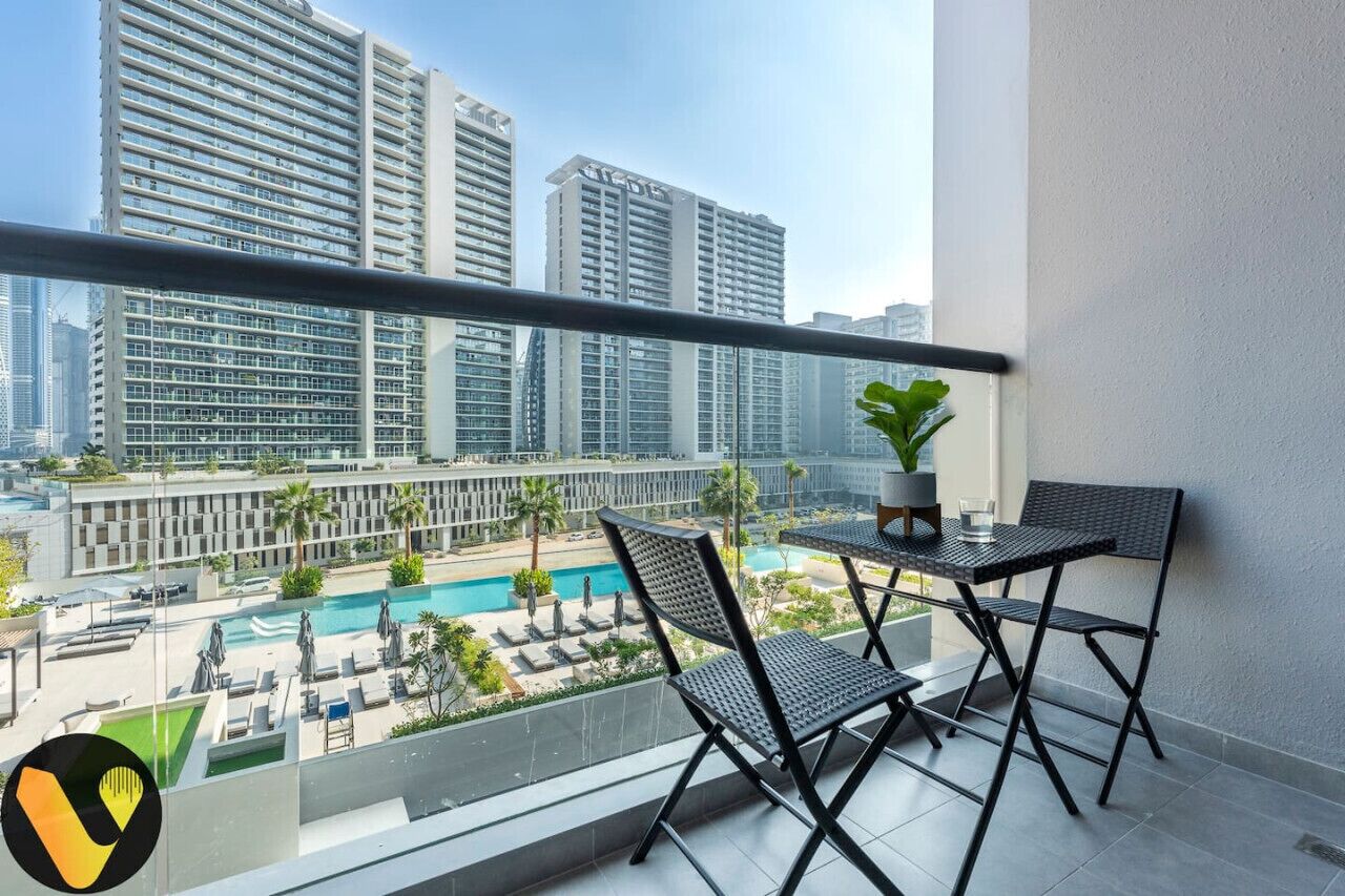 A balcony with two chairs and a table, overlooking a pool and high-rise buildings.