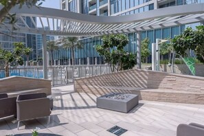 Un patio al aire libre con mobiliario moderno, una piscina y un edificio con grandes ventanales al fondo.