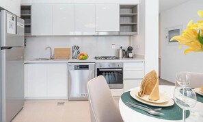 A modern kitchen with white cabinets, a dishwasher, a stove, and a dining area with a table set for two.