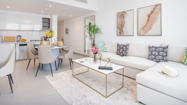 Een moderne woonkamer met een witte bank, een salontafel en een eethoek met stoelen, met een keuken op de achtergrond.