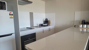 A modern kitchen with a stove, sink, and cabinets. There is a microwave above the stove, and a toaster on the counter. - Holiday In Husky by Book Jervis Bay - 2 Bedroom Apartment located in the centre of town (Huskisson)