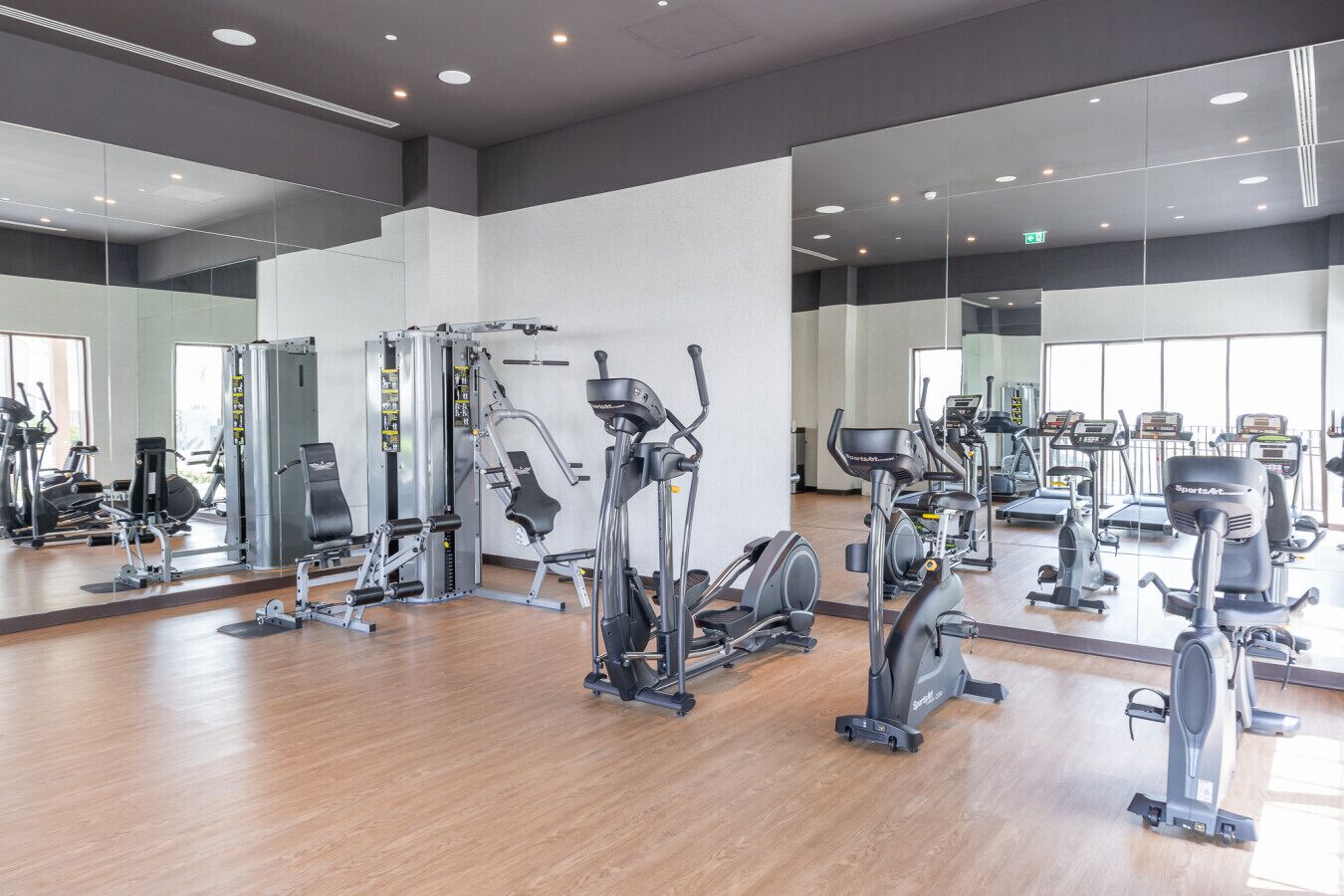 Een fitnessruimte met diverse trainingsapparaten, spiegels aan de wanden en houten vloeren.