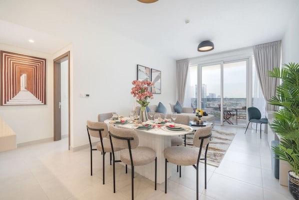 A modern dining area with a round table set for six, a large window with a city view, and a staircase leading to another level.