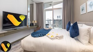 A modern hotel room with a large bed, a flat-screen TV, a city view, and a balcony.
