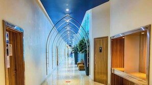 A hotel corridor with a polished floor, wooden doors, and a central plant.