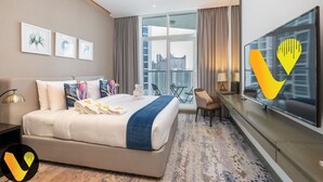Ein Hotelzimmer mit einem großen Bett, einem Fernseher, Blick auf die Stadt und gerahmten Kunstwerken an der Wand.