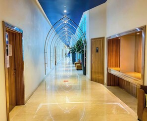 Un couloir d’hôtel avec un sol ciré, des portes en bois et une plante placée au centre.