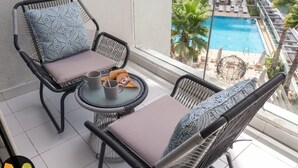 A balcony with wicker chairs, a small round table, and a view of a swimming pool.
