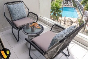 Un balcon avec des fauteuils en osier, une petite table ronde et une vue sur une piscine.