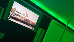 A room with a television displaying a Ferris wheel, green ambient lighting, a bed, and a small table. - AUTO HOTEL CONSTELACION  (Nacajuca)