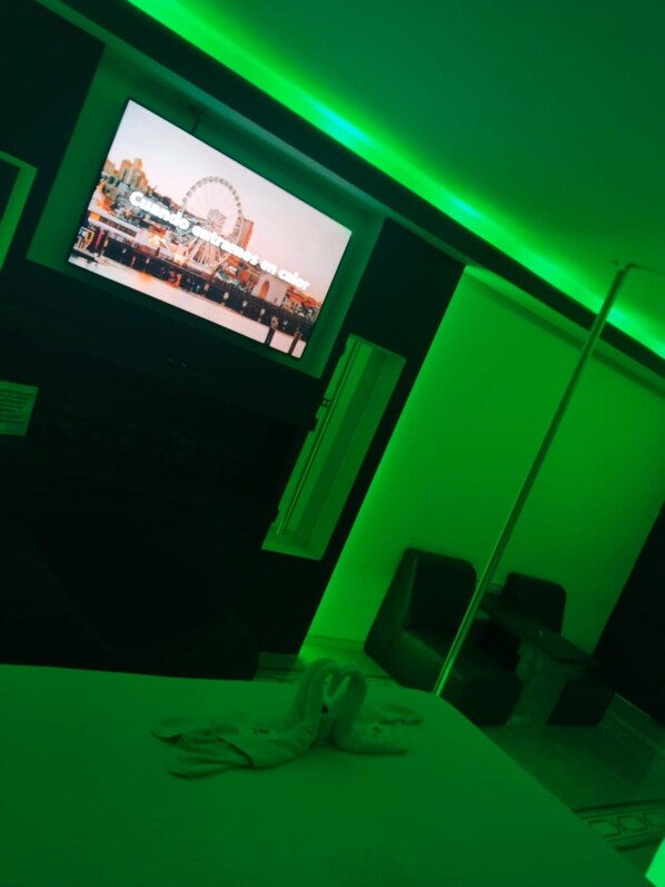 A room with a television displaying a Ferris wheel, green ambient lighting, a bed, and a small table.
