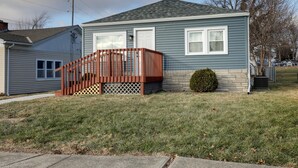 A single-story house with a wooden deck, a stone foundation, and a small bush. - Aunt Lele's Cozy Cottage (Quincy)