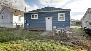 A single-story house with a front door, two windows, and a small front yard with a grill and chairs. - Aunt Lele's Cozy Cottage (Quincy)