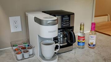 A Keurig coffee maker with a mug, a coffee pod holder, and two bottles of Torani syrup on a kitchen counter.
