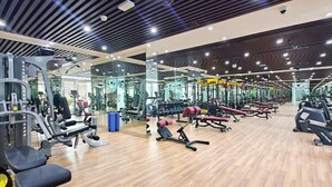 Un gimnasio con diversos equipos de ejercicio, paredes espejadas y suelo de madera.