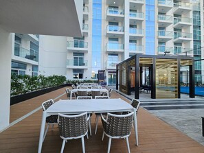 An outdoor dining area with tables and chairs, surrounded by a modern building with balconies.