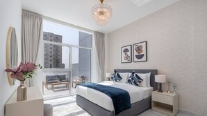 A modern bedroom with a large bed, a nightstand, a vase with flowers, and a view of the city through a large window. - Vogue, Al Furjan Pearlz by Danube near Ibn Battuta Mall (Dubai)