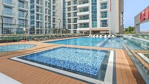 A rooftop swimming pool with a wooden deck, surrounded by high-rise buildings. - Vogue, Al Furjan Pearlz by Danube near Ibn Battuta Mall (Dubai)