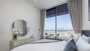 Un dormitorio moderno con una cama grande, un espejo redondo y vistas a un paisaje urbano a través de amplios ventanales.