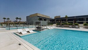 Una piscina en la azotea con sillones y sombrillas, rodeada de edificios modernos.