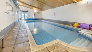 En inomhuspool med ett kaklat golv, ett träpanelat tak och en bänk längs väggen.