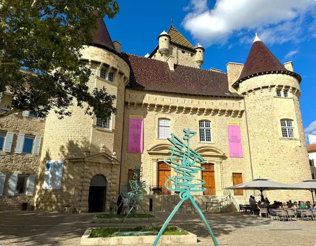 A historic stone building with a central courtyard, a prominent tower, and a decorative metal sculpture.