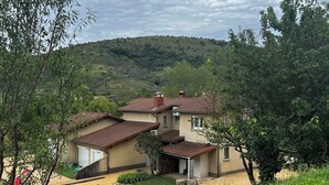 A house with a tiled roof, surrounded by greenery and a hilly landscape.