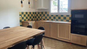 A kitchen with a wooden table, chairs, a Bosch refrigerator, a sink, and a window with a decorative iron grill.