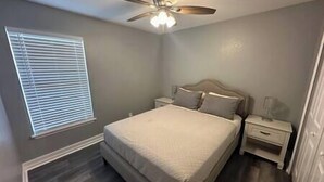A bedroom with a bed, nightstands, a ceiling fan, and a window with blinds.