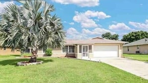 A single-story house with a garage, a well-maintained lawn, and a large palm tree.