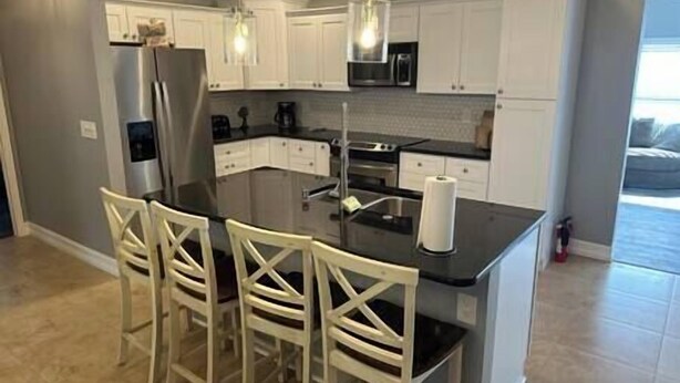 A modern kitchen with white cabinets, a black countertop, and a central island with bar stools.