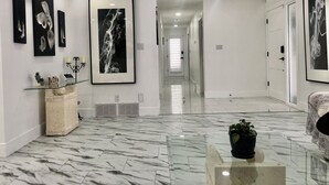 Un pasillo moderno con suelo de mármol, obras de arte enmarcadas en las paredes y una mesa de centro de cristal con una planta.