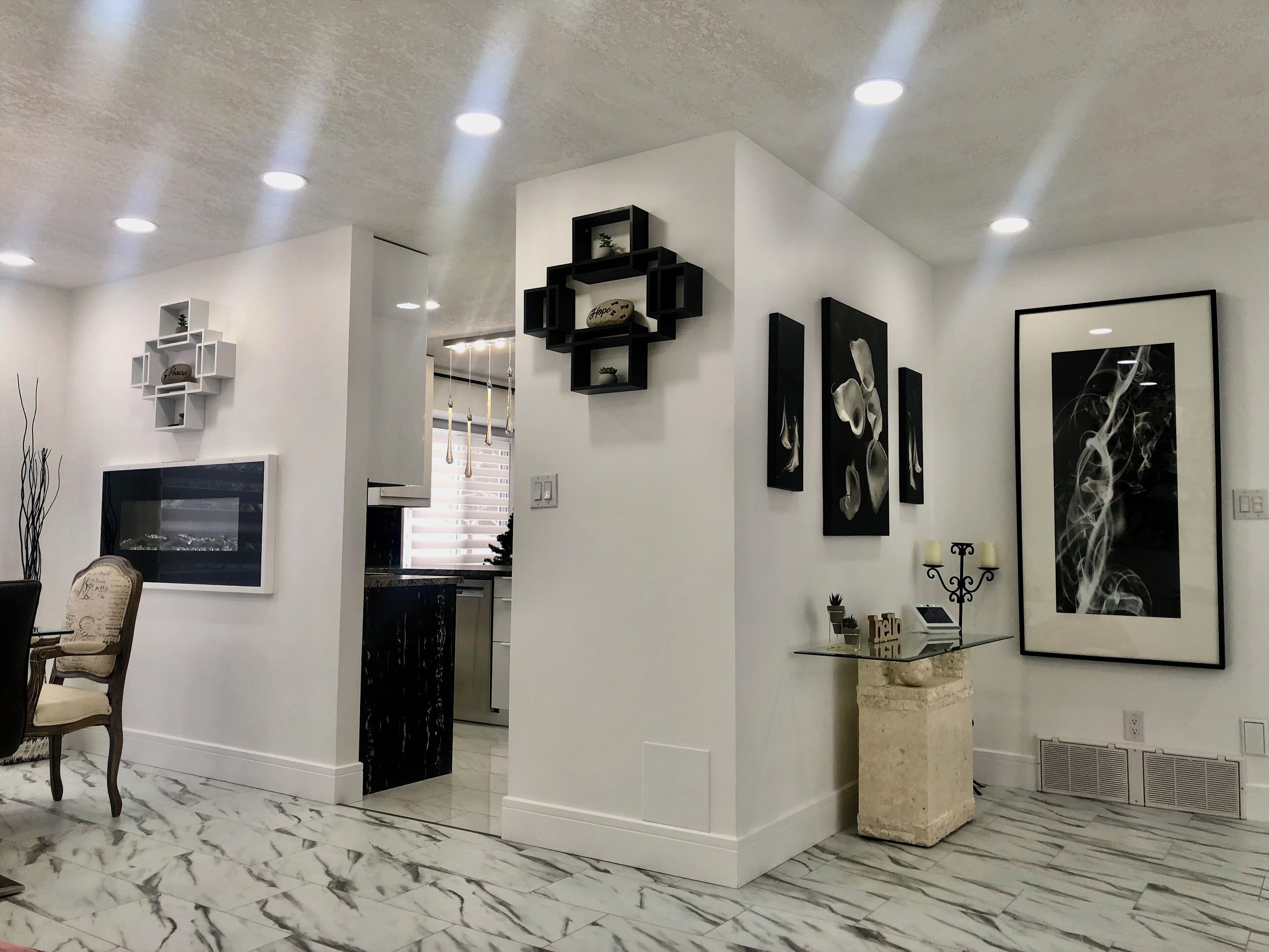 A modern interior with a marble floor, a dining area with a chair, a kitchen with a window, and artwork on the walls.