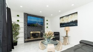 Una sala de estar moderna con chimenea, una mesa de centro de vidrio, un sofá y un televisor montado en una pared de ladrillo.