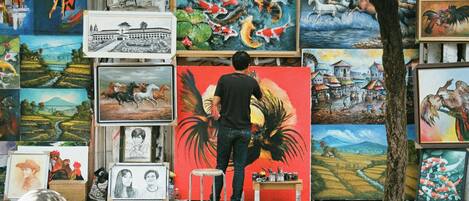 A street artist painting on a large canvas, surrounded by various artworks and paintings.