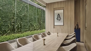 A conference room with a long table, chairs, and a view of a green wall with plants.